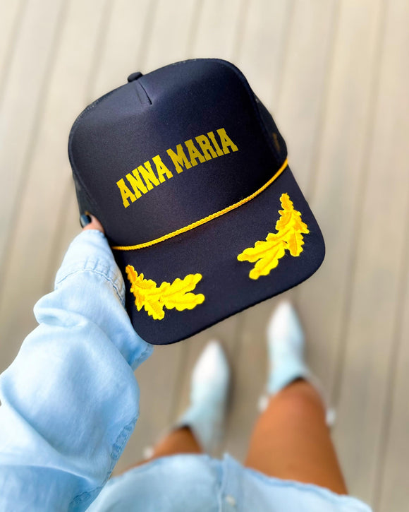 Anna Maria Island Florida black trucker hat with gold varsity lettering, gold rope and gold oak leaves on the visor