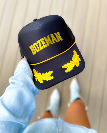 Bozeman Montana black trucker hat with gold varsity lettering, gold rope and gold oak leaves on the visor