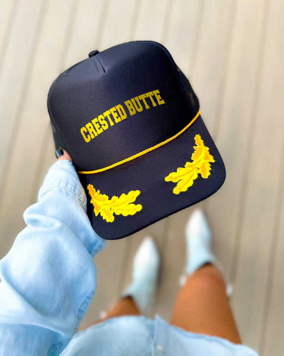 Crested Butte Colorado black trucker hat with gold varsity lettering, gold rope and gold oak leaves on the visor