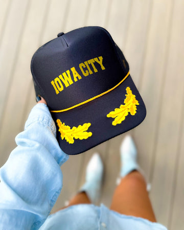 Iowa City Iowa black trucker hat with gold varsity lettering, gold rope and gold oak leaves on the visor